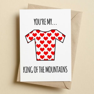 May include: A white greeting card with the text "YOU'RE MY... KING OF THE MOUNTAINS" in black. The card features a red heart-patterned cycling jersey illustration. The card is inside a brown envelope.