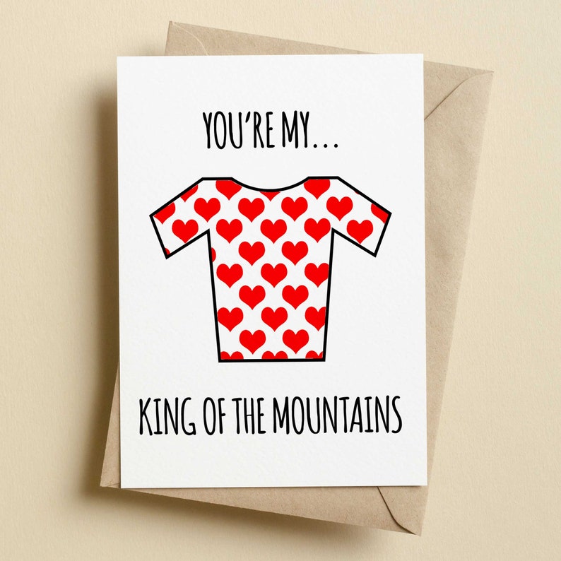 May include: A white greeting card with the text "YOU'RE MY... KING OF THE MOUNTAINS" in black. The card features a red heart-patterned cycling jersey illustration. The card is inside a brown envelope.
