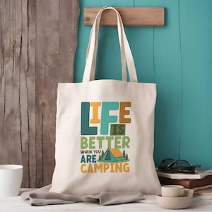 May include: Cream canvas tote bag featuring the slogan "LIFE IS BETTER WHEN YOU ARE CAMPING" in green, orange, and blue. The design includes a tent and trees. The bag has two handles.