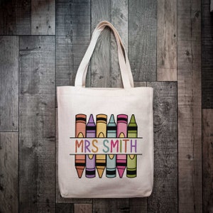 May include: A white canvas tote bag featuring a design of colourful crayons and the text "MRS SMITH" printed on it.