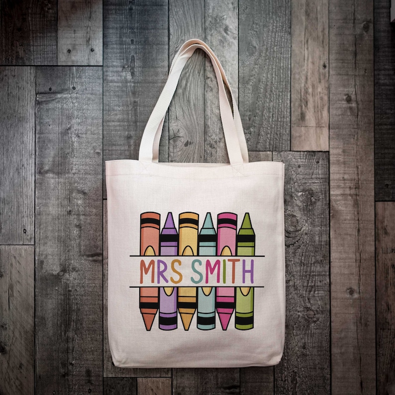 May include: A white canvas tote bag featuring a design of colourful crayons and the text "MRS SMITH" printed on it.
