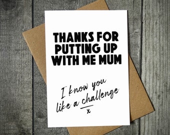 May include: A white greeting card with black text that reads: THANKS FOR PUTTING UP WITH ME MUM. Below this, in a smaller, cursive-style font, it says: I know you like a challenge x. The card is placed on top of a brown kraft paper envelope.