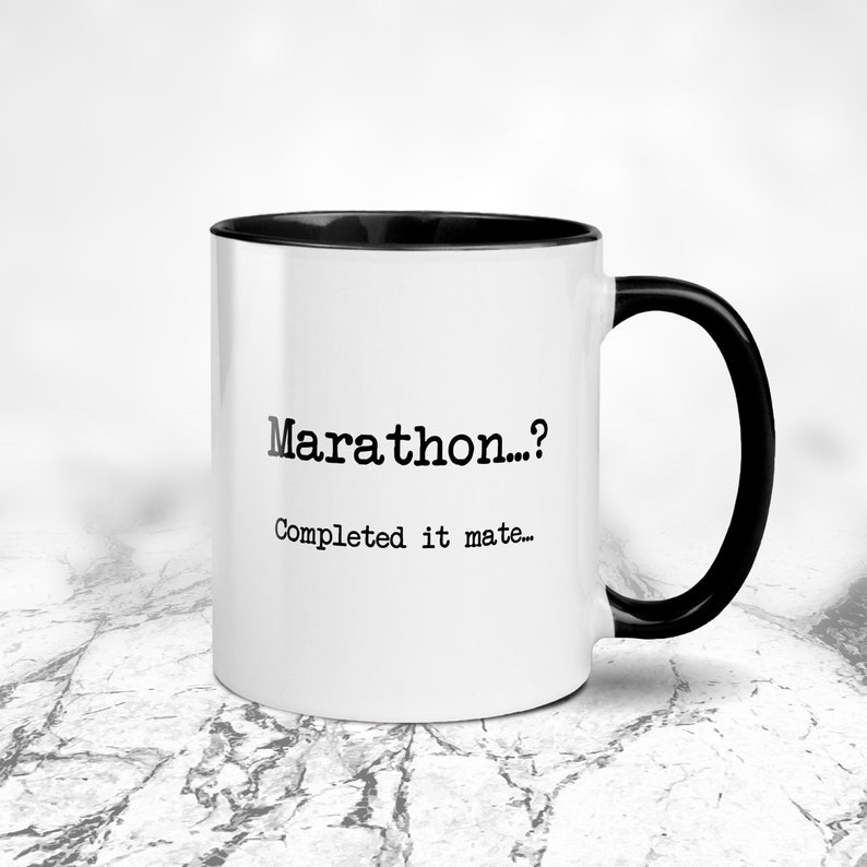 K&ouml;nnte beinhalten: Wei&szlig;er Keramikbecher mit schwarzem Innenraum und Henkel. Der Becher tr&auml;gt den Text "Marathon...?" &uuml;ber "Completed it mate..." in schwarzer Schrift. Auf einer marmor&auml;hnlichen Oberfl&auml;che.