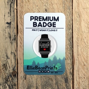 May include: A white round pin badge with a black and gray smartwatch graphic. The smartwatch screen displays the text "IF I COLLAPSE PLEASE PAUSE MY WATCH!" with a red heart icon. The badge has the text "PREMIUM BADGE PIN IT | WEAR IT | LOVE IT" and "Ellie Bean Prints EST. 2011" printed on it.