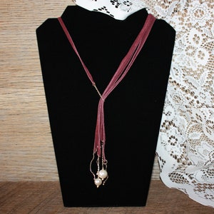 May include: A long burgundy suede necklace with two large white pearl accents.