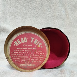 May include: A red and white tin container with the text "READ THIS" and "MICA AXLE GREASE" on the lid. The text reads "do not think because your Axle LOOKS dry that it is dry. The powdered Mica that is in the Grease gives it that appearance. Run your finger over the Axle and you will find plenty of Grease. Mica is in itself a SPLENDID LUBRICANT."