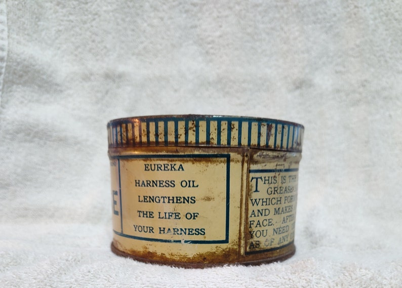 May include: A vintage tin can of Eureka Harness Oil. The label reads "Eureka Harness Oil Lengthens The Life Of Your Harness" and "This is the grease which for and makes face. After you need ab of any".