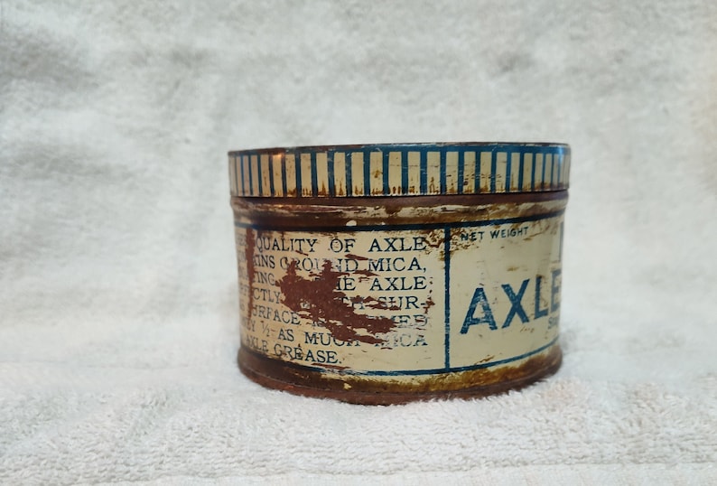 May include: A vintage tin can of axle grease with blue and white striped lid and label that reads "QUALITY OF AXLE GREASE, CONTAINS GROUND MICA, PERFECTLY SMOOTH SURFACE, AS MUCH WEAR AS ANY AXLE GREASE. NET WEIGHT 1 LB. AXLE GREASE".
