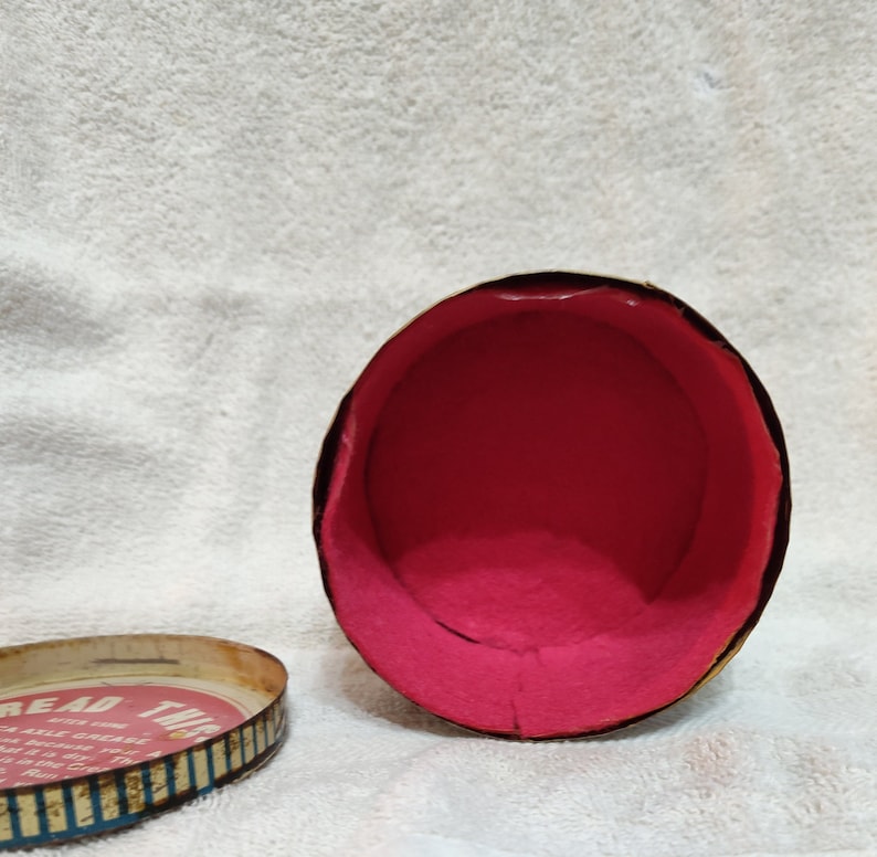 May include: An empty, round, vintage tin container with a pink interior. The lid is off and shows the text "Bread  Twis" with a graphic of a braid of bread.