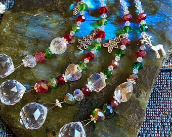 May include: Three crystal suncatchers with red, green, and clear beads, and silver charms. The suncatchers are hanging from a rock.