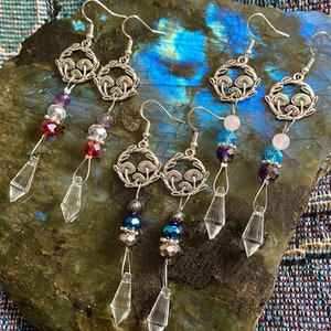 May include: Three pairs of silver earrings with crystal and gemstone accents. Each pair features a circular charm with a mushroom design and a dangling crystal teardrop.