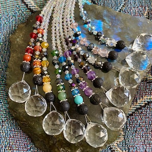 May include: A set of 10 crystal suncatchers with rainbow colored beads and lava rock accents. Each suncatcher features a clear crystal prism and is strung with beads in a variety of colors, including red, orange, yellow, green, blue, indigo, and violet. The suncatchers are hung from a silver string.