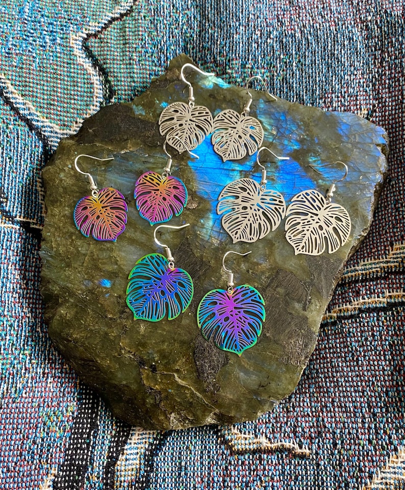 Pu&ograve; includere: Un set di sei orecchini iridescenti con un design a foglia tropicale. Gli orecchini sono in metallo e hanno una finitura argentata. Le foglie sono ritagliate e hanno un design delicato e intricato.