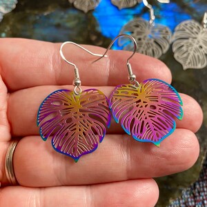 Pu&ograve; includere: Un paio di orecchini a forma di foglia di monstera arcobaleno iridescente con ganci d'argento.