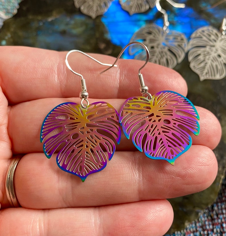 Pu&ograve; includere: Un paio di orecchini a forma di foglia di monstera arcobaleno iridescente con ganci d'argento.