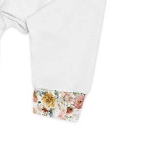 Op de afbeelding: Wit overhemd met lange mouwen en een manchet met bloemenprint. De manchet heeft een verscheidenheid aan roze, gele en oranje bloemen.