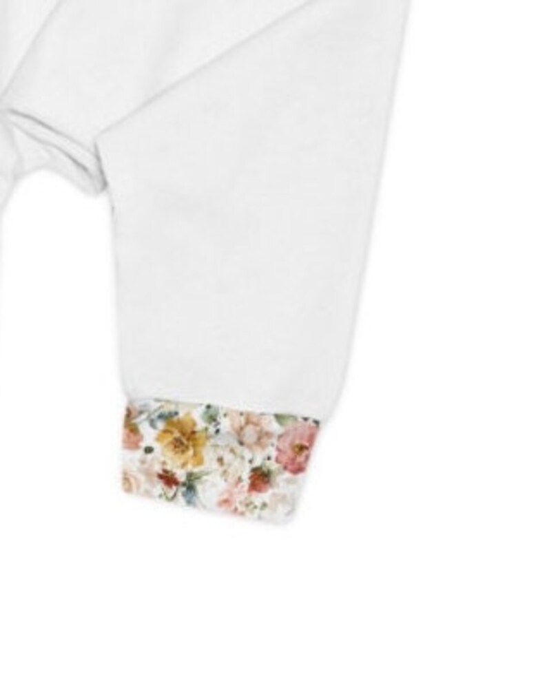 Op de afbeelding: Wit overhemd met lange mouwen en een manchet met bloemenprint. De manchet heeft een verscheidenheid aan roze, gele en oranje bloemen.