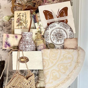 May include: An assortment of vintage-style items, including a woven bag, decorative plates, cards with butterfly and floral designs, a small vase, and a decorative butterfly. The color palette includes beige, brown, and white.