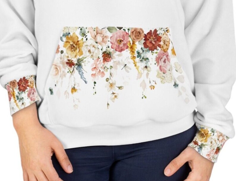 Op de afbeelding: Witte hoodie met een bloemenprint op de zak en de manchetten. De bloemen zijn in tinten roze, geel en rood.