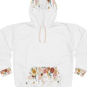 Op de afbeelding: Witte hoodie met een bloemenprint op de capuchon, manchetten en zak. De print bevat een verscheidenheid aan bloemen in tinten roze, geel en oranje.