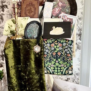 May include: An assortment of vintage-inspired decor items, including a swan illustration, framed floral prints, a velvet green fabric, and a gold candlestick. A woven bag and a postcard are also visible.