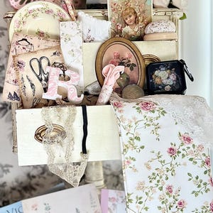 May include: A collection of vintage-style items, including a pink butterfly, floral-patterned plates, fabric, and artwork. The color palette is soft, featuring pinks, creams, and greens, creating a romantic and feminine aesthetic.