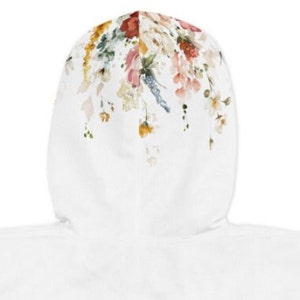 Op de afbeelding: Witte hoodie met een bloemenprint op de capuchon. De print bevat verschillende bloemen in tinten roze, rood, geel en blauw.