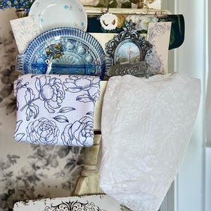 May include: A display of vintage decor items, including a silver gravy boat, blue and white china, floral artwork, and a sign that reads "Powder Room." A white lace fabric and a star-patterned cloth are also visible.