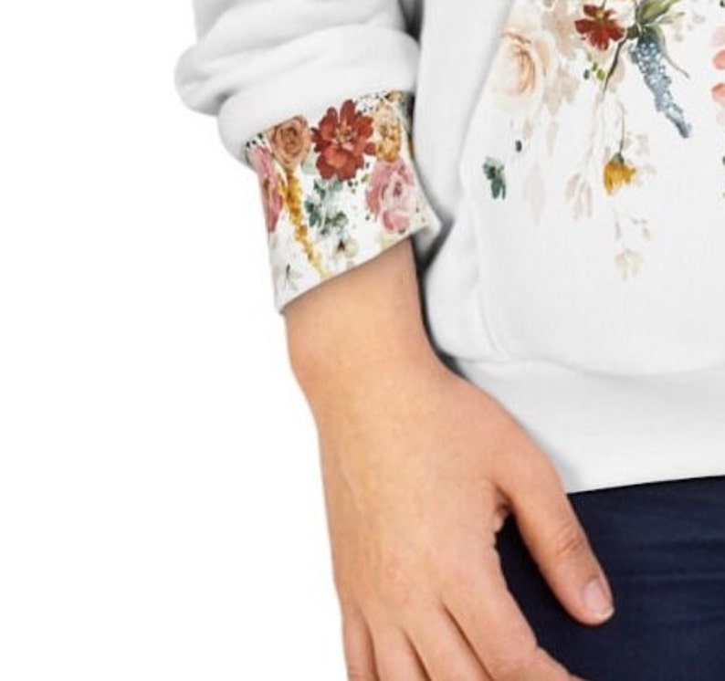 Op de afbeelding: Witte hoodie met een bloemenprint op de voorkant en de manchetten. De bloemenprint heeft roze, rode en gele bloemen.