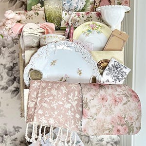 May include: A display of vintage-style items, including floral-patterned plates, a green glass bottle, and a clutch with a butterfly design. The backdrop features a floral wallpaper, creating a cohesive aesthetic.