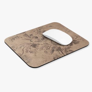 May include: A rectangular mouse pad with rounded corners featuring a tan and brown floral pattern. A white computer mouse rests on the surface of the mouse pad, which has a black edge trim.