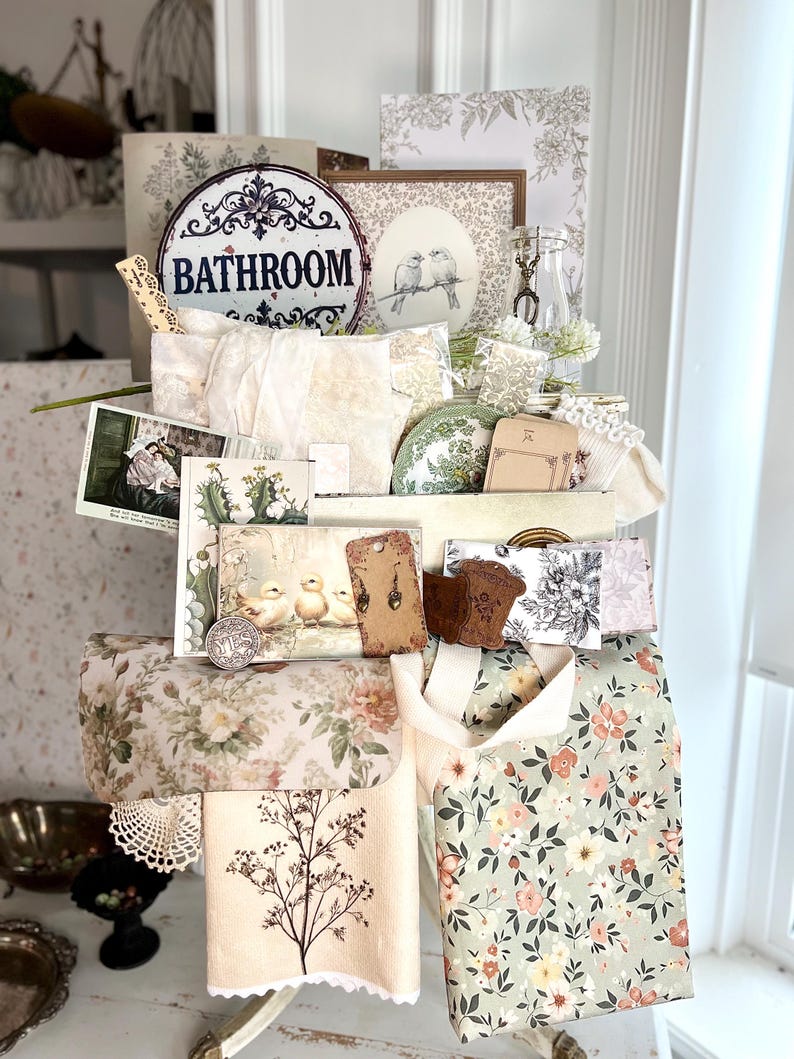 May include: A collection of vintage-style items, including floral-patterned fabric, decorative cards, and a metal sign that reads "Bathroom." The items are arranged on a white surface, creating a charming, nostalgic aesthetic. The color palette includes soft pastels and muted tones.