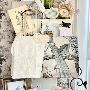 May include: A collection of vintage-style decorative items, including a framed blue bird print, a white lace cloth, a green glass bottle, and a floral patterned mug. Other items include a small gold framed picture, a decorative plate, and a butterfly print.