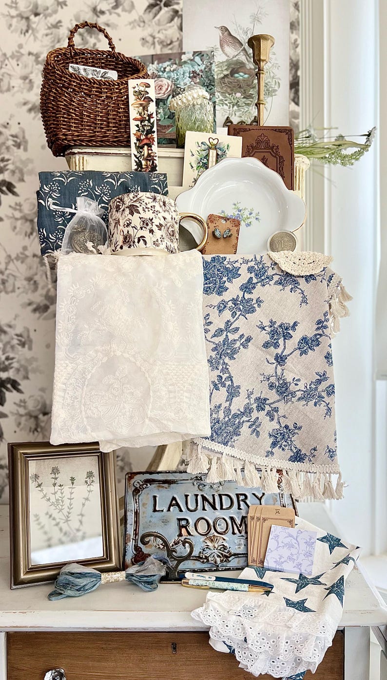 May include: A collection of vintage-style home decor items, including a woven basket, floral-patterned fabric, a framed botanical print, and a metal "LAUNDRY ROOM" sign. The color palette includes white, blue, brown, and gold tones, creating a rustic and charming aesthetic.