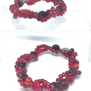 May include: Two red and black beaded bracelets with silver clasps. The bracelets are made with small red beads, larger red beads, and black beads.