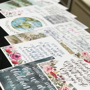May include: A collection of watercolor art prints featuring calligraphy and floral accents. The prints display inspirational quotes and Bible verses, with a focus on faith and encouragement. The color palette includes blues, pinks, and greens.