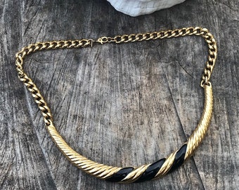 May include: A gold chain necklace with a black and gold twisted pendant. The pendant is a curved shape with a black enamel design.