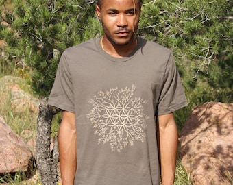 May include: A person wearing a dark gray t-shirt with a gold geometric design. The design features a flower of life pattern with branches extending outward.