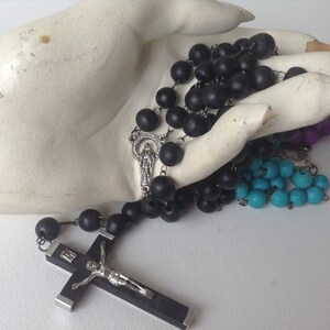 Puede incluir: Un rosario de madera negra con un crucifijo de plata y un dije de plata con la Virgen Mar&iacute;a. El rosario se muestra en una mano blanca.
