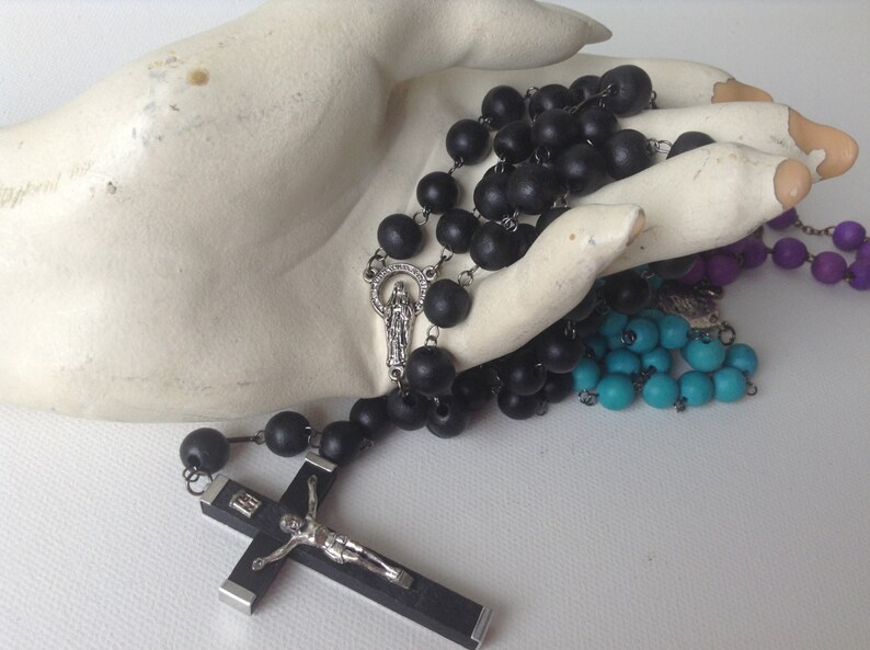 Puede incluir: Un rosario de madera negra con un crucifijo de plata y un dije de plata con la Virgen Mar&iacute;a. El rosario se muestra en una mano blanca.