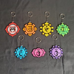 May include: Seven colourful chakra keychains with beaded designs. Each keychain features a different colour and symbol representing the seven chakras.