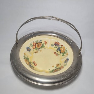 Könnte beinhalten: Eine antike Servierplatte mit Blumenmuster, silberfarbenem Rand und einem Griff. Die Platte hat einen gelben Hintergrund mit einem Blumenmuster in Blau-, Orange- und Gelbtönen.
