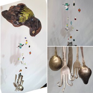 Puede incluir: Un móvil hecho de madera flotante, cuentas de vidrio y cucharas de metal. La madera flotante está pintada con un diseño de helecho verde. El móvil está colgado del techo y está decorado con cuentas de vidrio de colores y cucharas de metal.