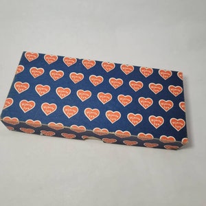 May include: A blue box with a repeating pattern of red hearts that say "Hjärta Lys" in white lettering.