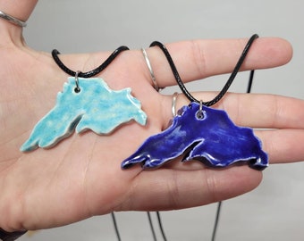 May include: Two ceramic necklaces shaped like the outline of Lake Superior. One necklace is blue and the other is teal.