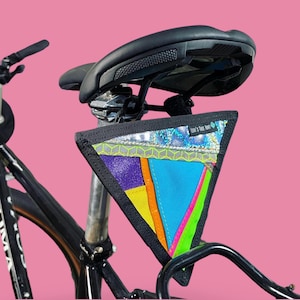 Könnte beinhalten: Ein schwarzes Fahrrad mit einer bunten, geometrisch gemusterten dreieckigen Tasche, die am Sattelpfosten befestigt ist. Die Tasche trägt den Schriftzug "Levi's Tree Farm".