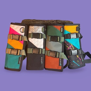 Puede incluir: Cuatro bolsas de tela coloridas con correas y hebillas ajustables. Cada bolsa tiene un patrón geométrico y una combinación de colores diferentes, incluyendo turquesa, naranja, negro, blanco, verde y amarillo. Las bolsas están etiquetadas con "Love is True Love".