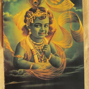 May include: A painting of a young boy with blue skin, wearing a yellow and gold robe and a jeweled crown. He is holding a flute and has a peacock feather in his hair.