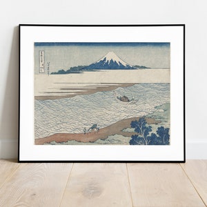 Puede incluir: Una impresión japonesa vintage en madera de la montaña Fuji, una montaña cubierta de nieve, elevándose sobre un mar agitado con un pequeño bote en primer plano. La impresión está enmarcada en negro y tiene texto japonés en la esquina superior izquierda.