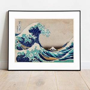 Puede incluir: Una impresión japonesa en madera enmarcada que representa una gran ola rompiendo sobre tres barcos. La ola es azul y verde con espuma blanca. El fondo es de color beige claro. La impresión está titulada "La Gran Ola de Kanagawa" en japonés.